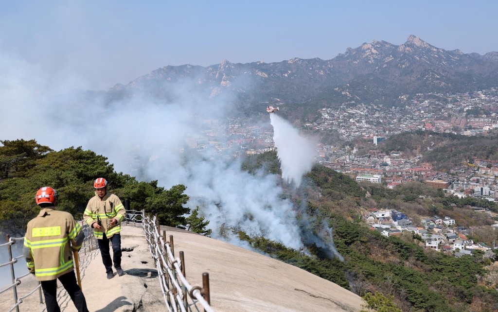 Firefighters watching as a helicopter douses a wildfire on Mount Inwang in Seoul.