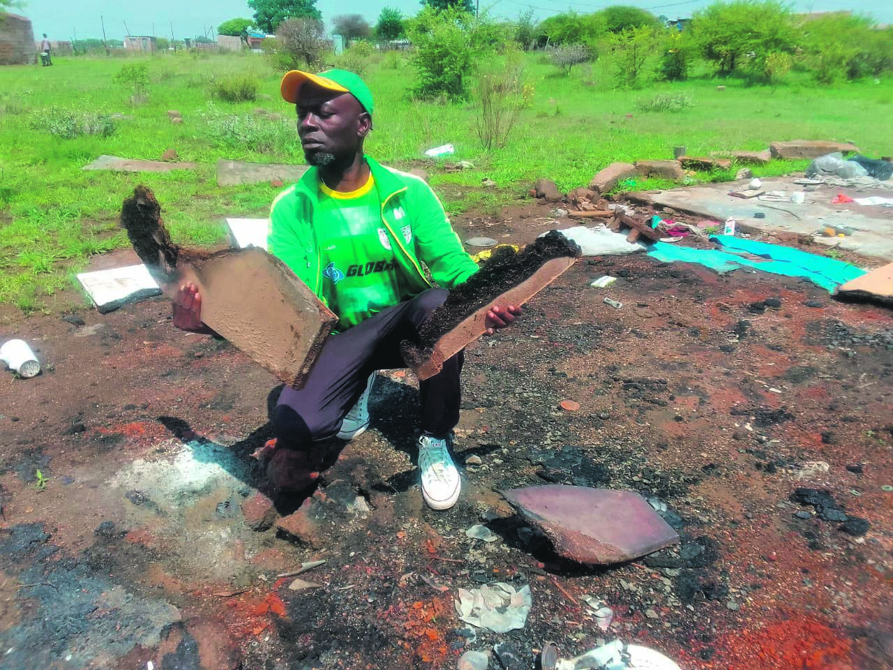 Community leader Shangy Mbekwa holding the remains of wooden coffins that were burnt by community members a month after they were discovered abandoned in a shack. Photo by Raymond Morare
