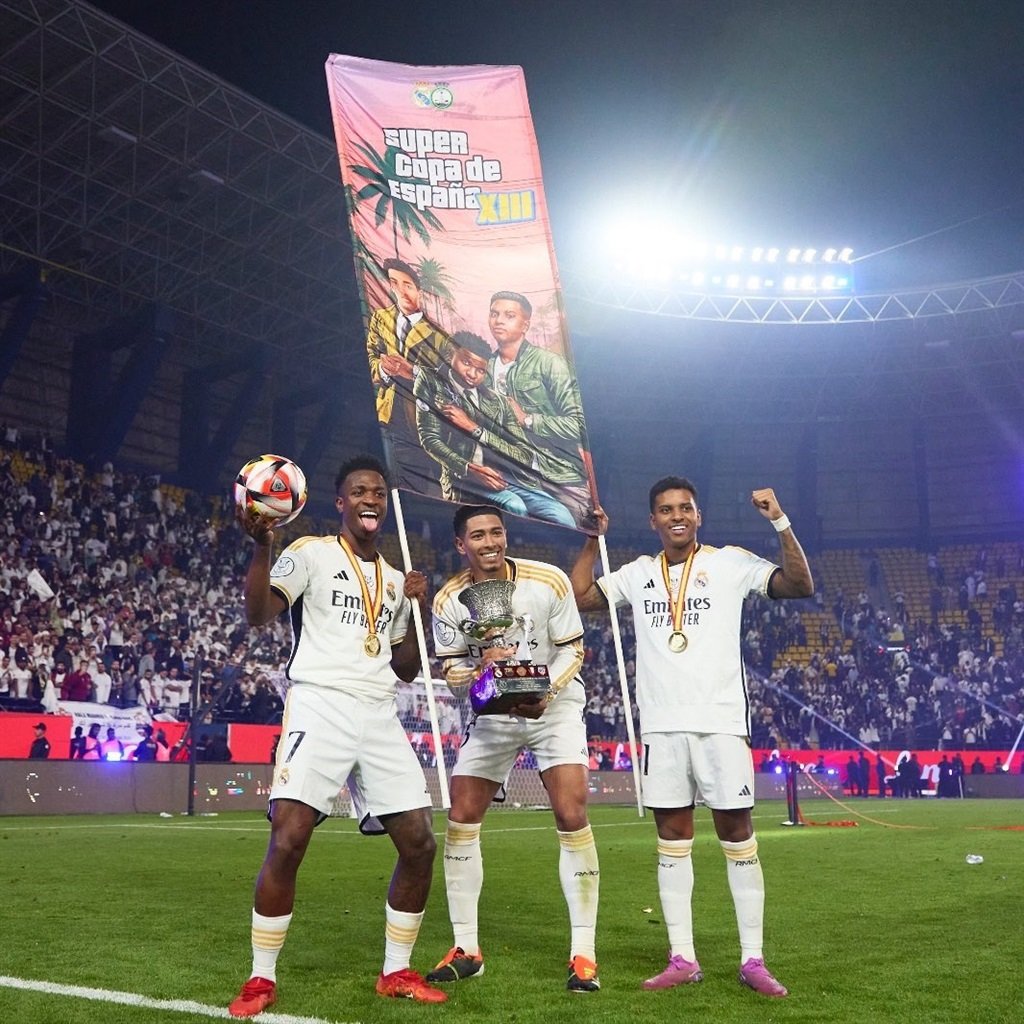 Real Madrid stars Jude Bellingham, Vinicius Jr, and Rodrigo holding up their GTA 6 banner.