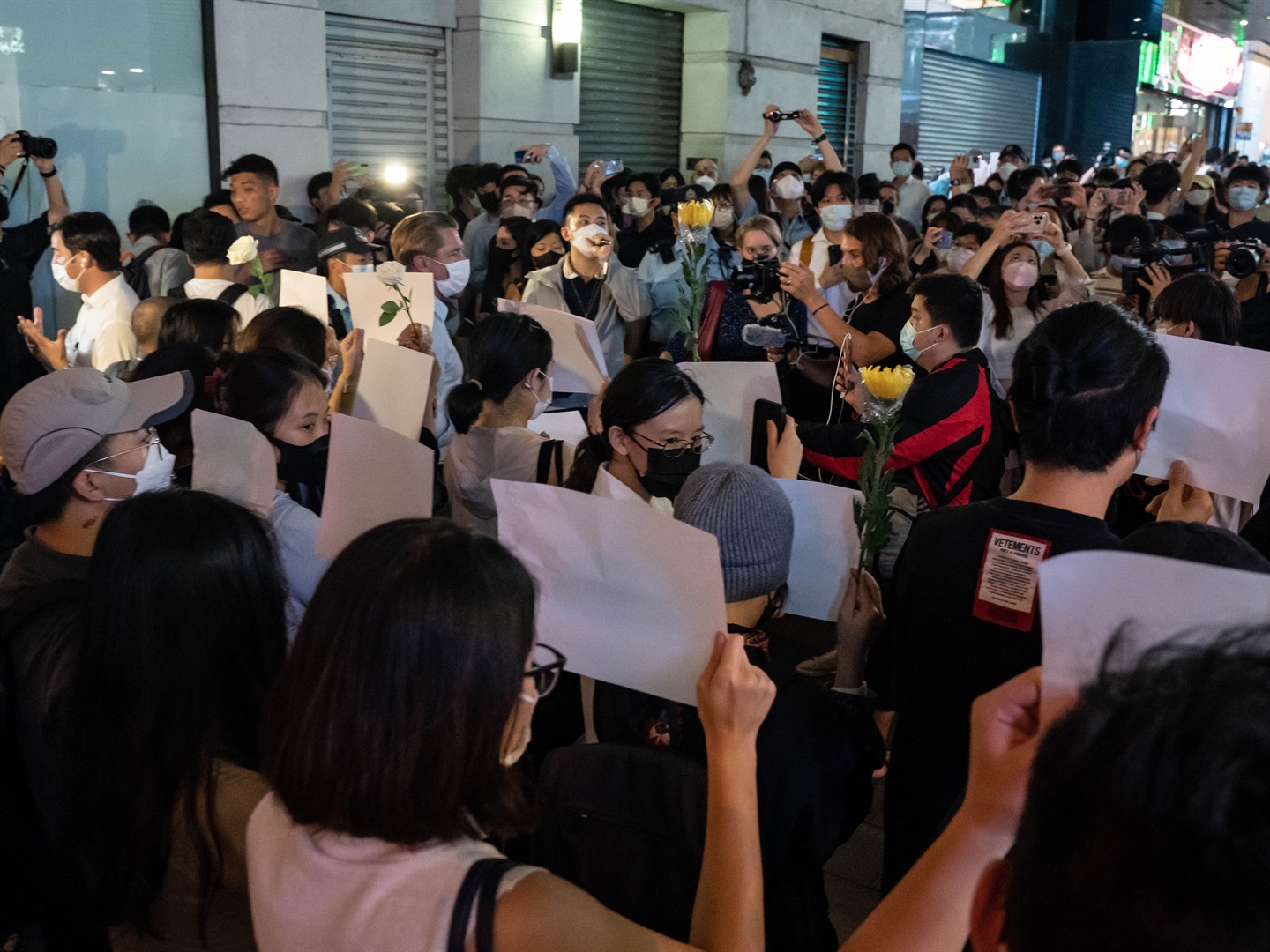 People hold sheets of blank paper and flower in protest of COVID restriction in mainland as police setup cordon during a vigil in the central district on November 28, 2022 in Hong Kong, China.