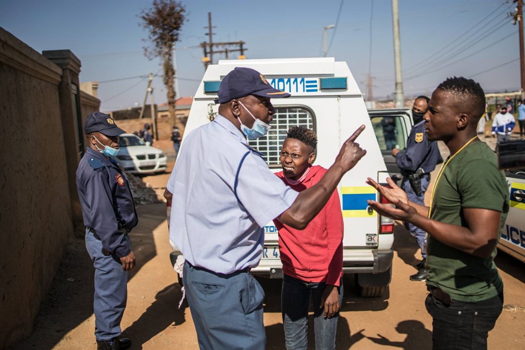 An SAPS officer gestures at a man pleading for the release of a protester detained for breaching the lockdown regulations on 13 May 2020 during a protest in Snake Park, Soweto.