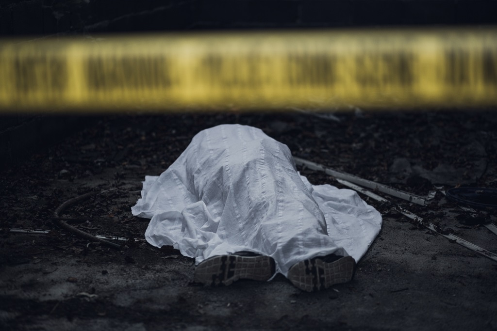 The dead body is seen lying on the ground behind a cordon tape.