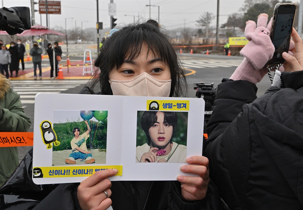 A fan holds pictures of BTS singer Jin in front of