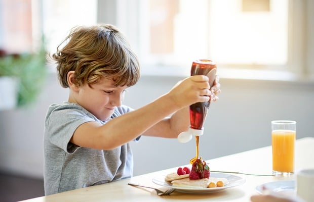 boy pouring syrup over pancakes