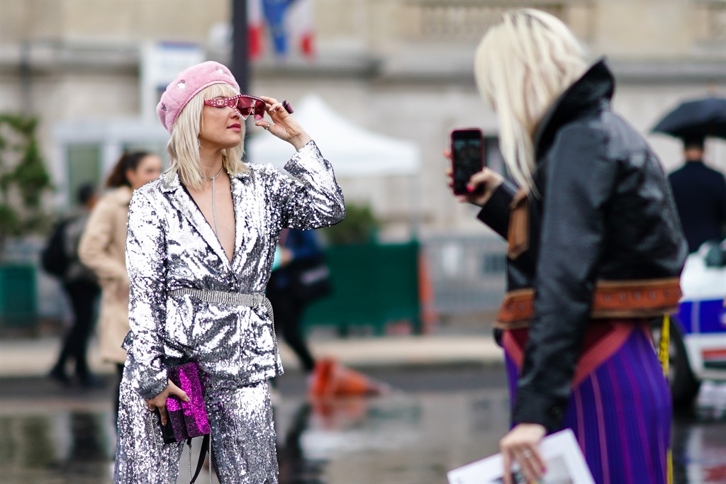 A guest wears a pink beret hat, red sunglasses, a silver shiny glitter outfit, a purple clutch, a necklace, and is posing for a selfie, outside Chanel, during Paris Fashion Week - Womenswear Spring Summer 2020, on October 01, 2019 in Paris, France. (Photo by Edward Berthelot/Getty Images)