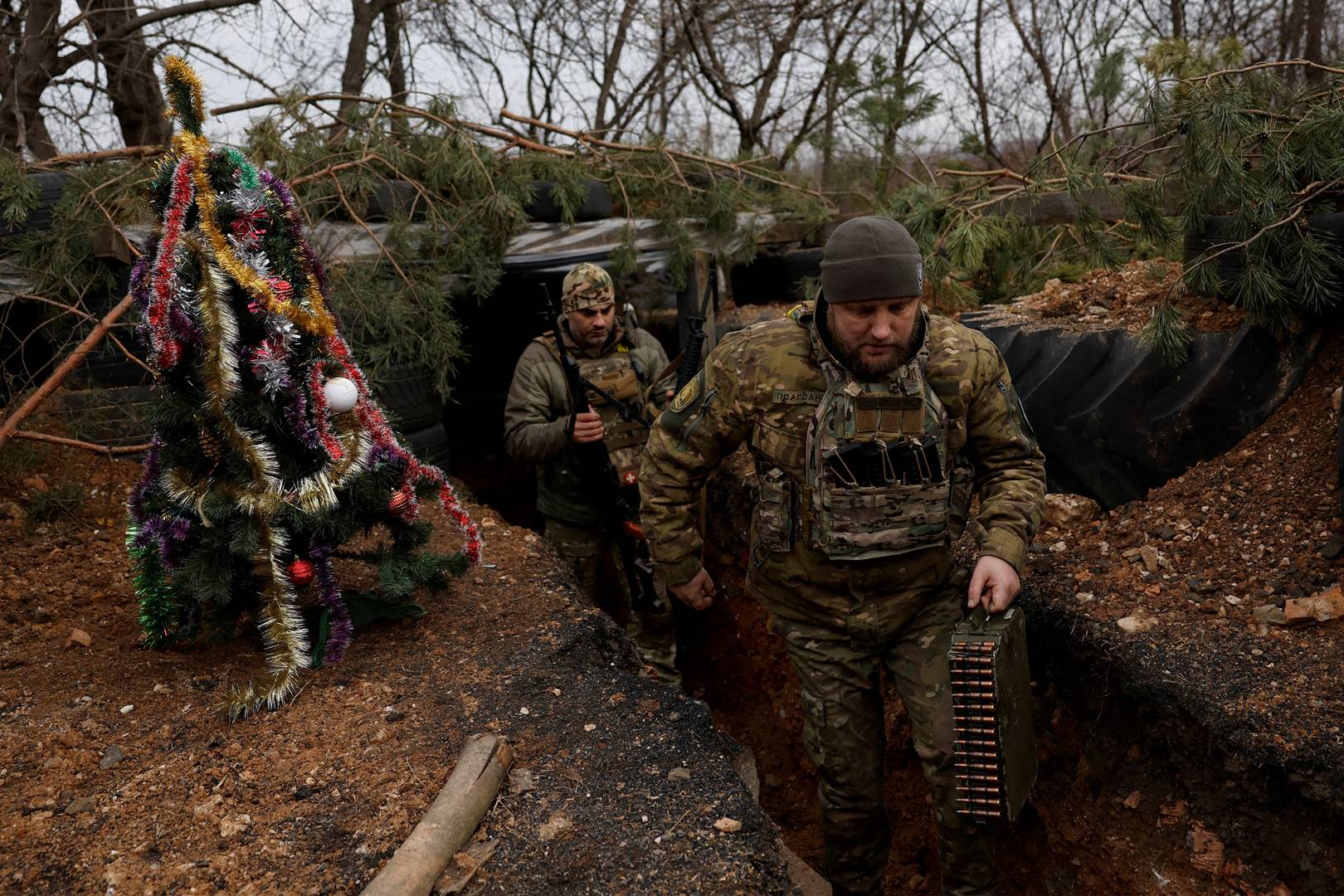 24 Desember, Bachmoet, Oekraïne | Gewapende Oekraïense soldate van die Dnipro 1- spesiale taakmag stap in ’n loopgraaf verby ’n Kersboom. Foto: Reuters