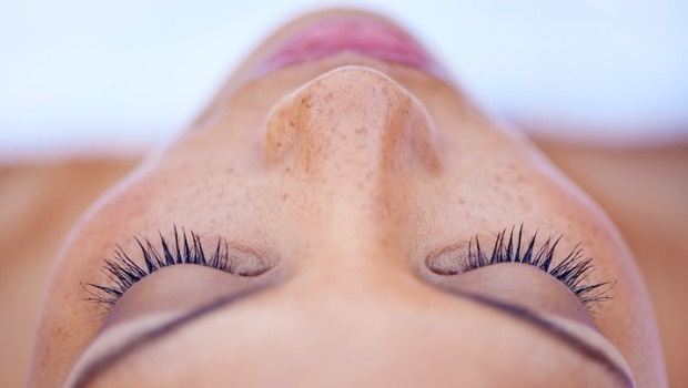 A woman closes her eyes to get her lash extensions applied