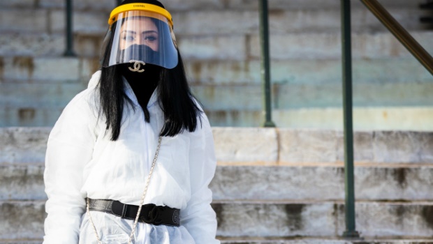 A guest, wearing white nonwoven coverall, Chanel mask, belt and bag full of hand sanitizer, is seen outside the Chanel show during Paris Fashion Week. Due to a sharp increase in the number of cases of coronavirus (COVID-19) declared in Paris and throughout France, several sporting, cultural and festive events have been postponed or canceled. Photo by Claudio Lavenia/Getty Images
