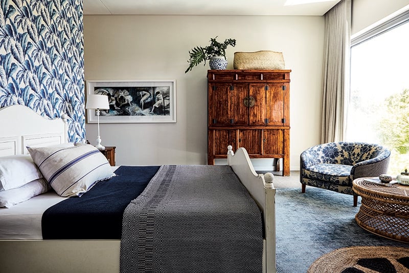 Striking blue-and-white wallpaper makes a style statement in this spacious room. The bathroom is located behind the eye-catching focal wall. Tropica wallpaper in the colour Delft from Hertex; blankets and oversized pillow from Mungo Design, chair upholstery fabric and rugs from Hertex