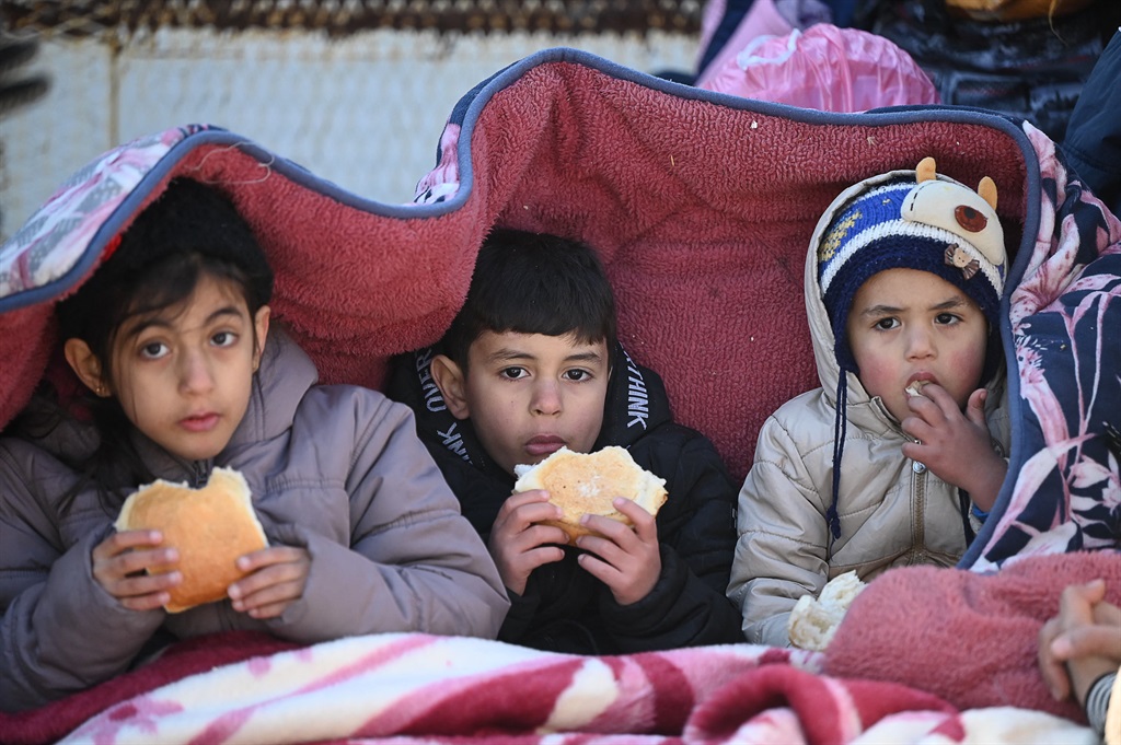 Children eat bread as they sit under a cover in th