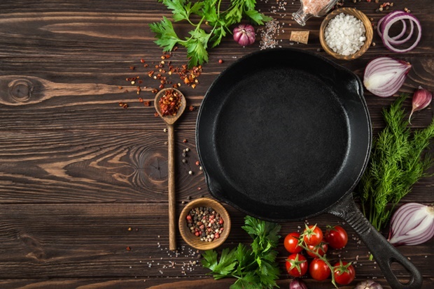 herbs and spices around cast iron skillet on woode