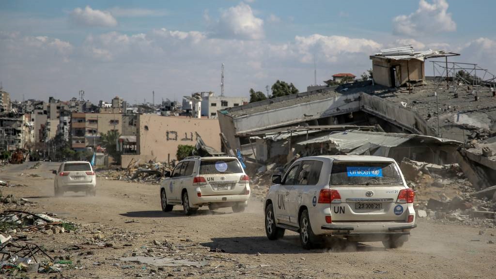 UN vehicles drive amid buildings destroyed in prev