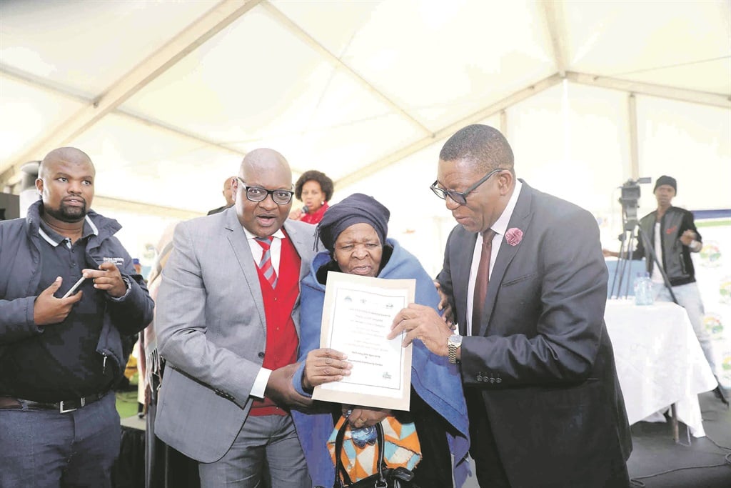 Gauteng Premier David Makhura and Dikgang Moiloa, the MEC for human settlements,       cooperative governance and traditional affairs, hand over a title deed to Layekile Modisang in Impumelelo, Devon