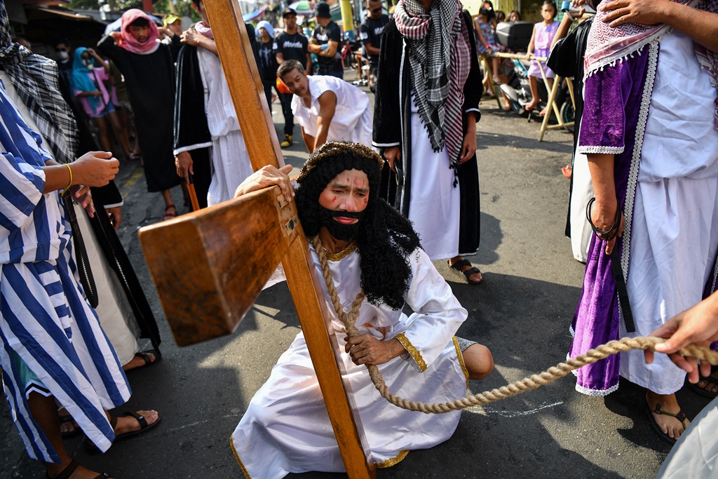 An actor portraying Jesus carries a cross during a