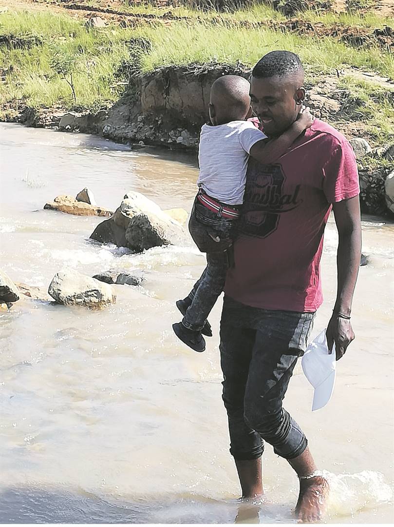 Luvuyo Nyangiwe carries his son Liqhame across the Mgxojeni River, where his daughter and five other pupils were washed away and drowned near Mount Fletcher last week. Picture: Lubabalo Ngcukana/City Press
