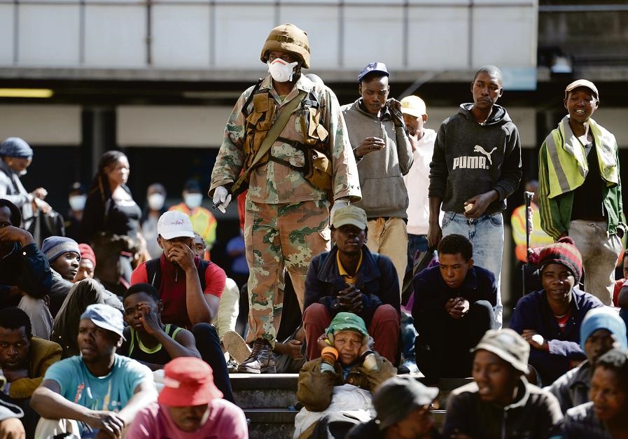 ’n Soldaat staan by hawelose mense wat Vrydag in die Johannesburgse middestad bymekaargemaak is nadat Suid-Afrika se  21 dae van inperking die vorige nag in werking getree het.   Foto: AP