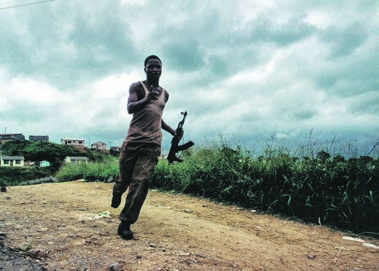 An Inkatha Freedom Party supporter runs back from the dividing line between political factions after emptying his AK-47 ammunition clip at the homes of ANC supporters in Umlazi Township Picture: Greg Marinovich 