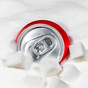 Soft drinks can sitting in sugar like an iceberg, illustrating social issue of excess sugar in foods.
