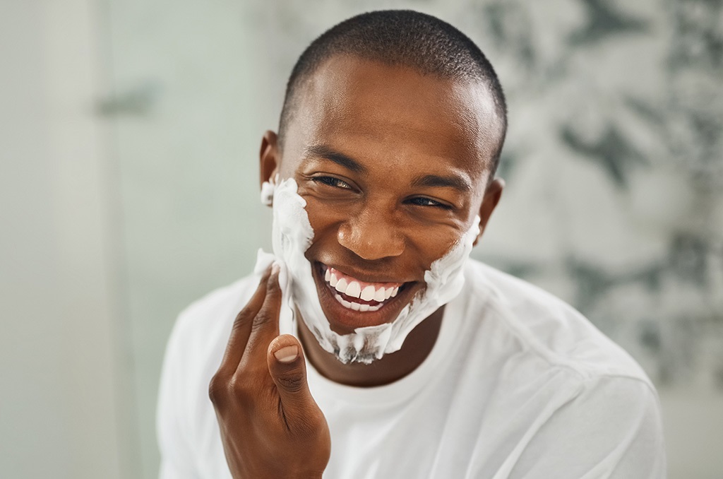 A young man shaves his facial hair in the bathroom.