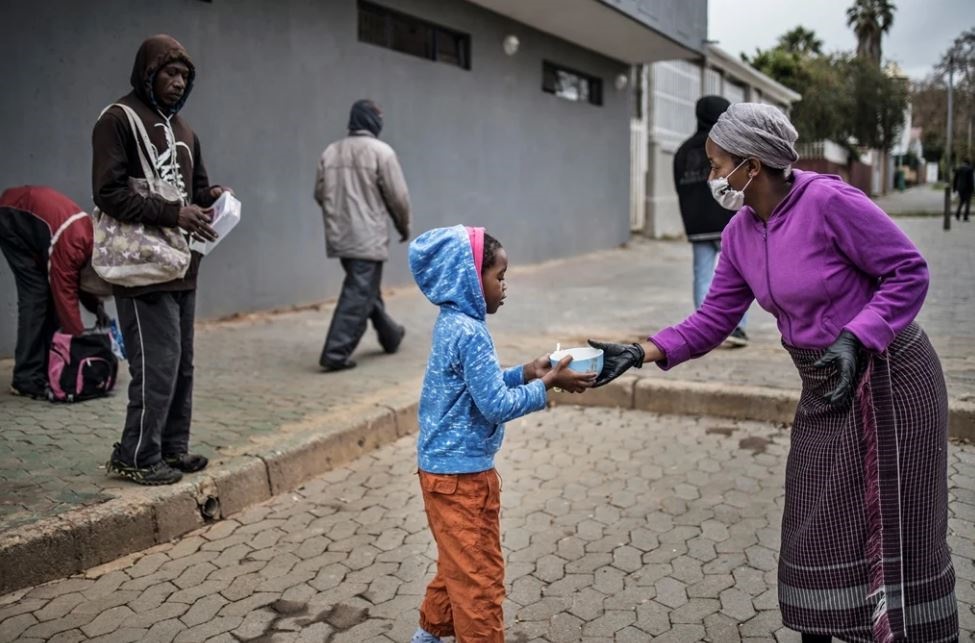 A volunteer for the grassroots charity, Hope for Vrededorp, hands over a warm meal to a child at a daily food distribution in the impoverished district of Vrededorp in Johannesburg as the country remains under lockdown. 
