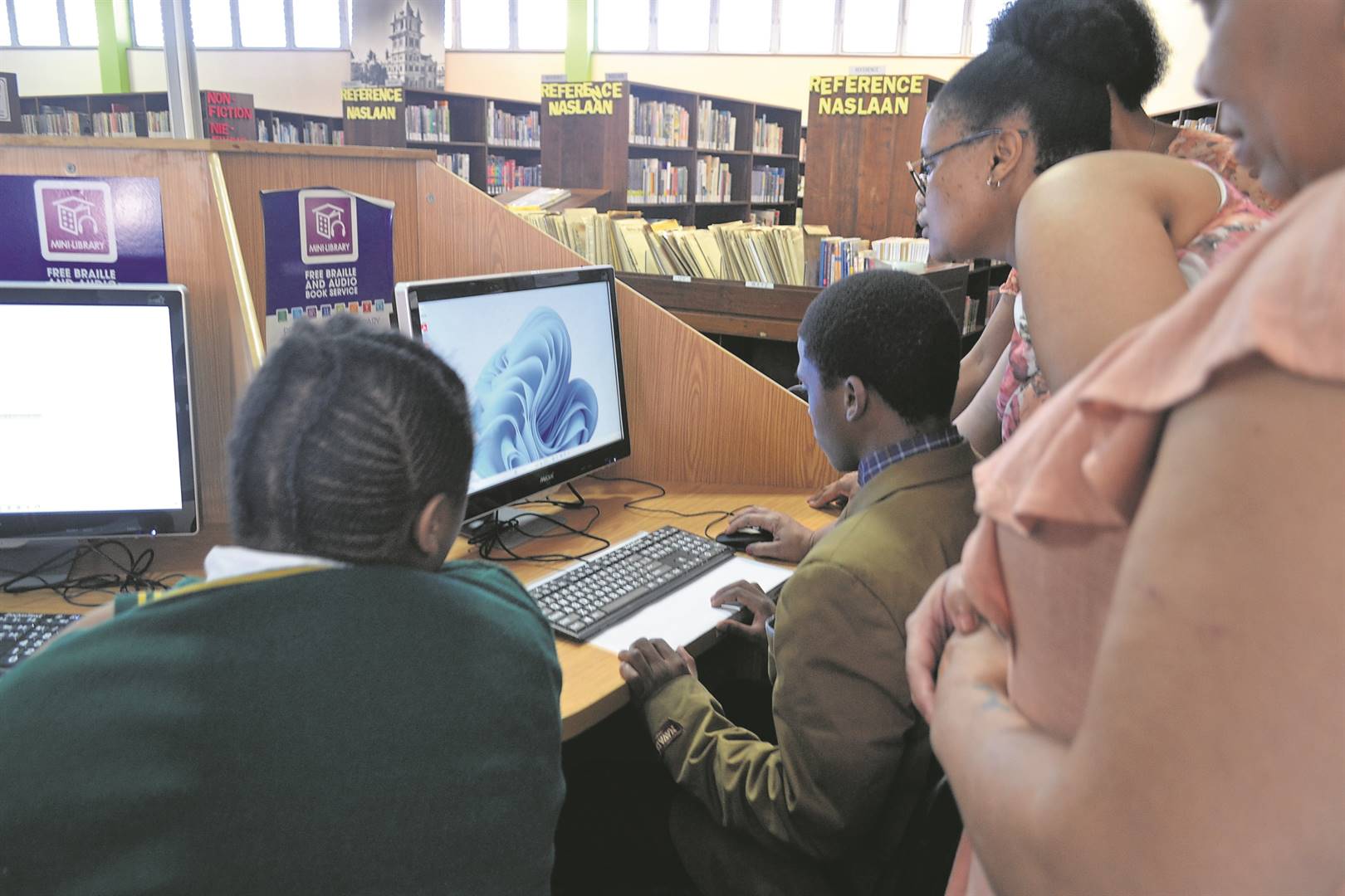 Nomfundiso Mka, a library assistant at Uitenhage Library shows the Khanyisa learners how to use the e-reader (left) and the two computer stations in the mini-library.                             