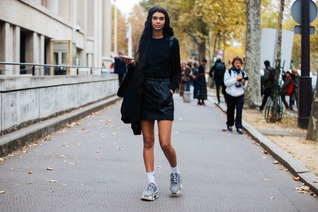 Model Jordan Daniels wears a black top, black leather skirt, white Nike socks, and blue Balenciaga sneakers after the Miu Miu show during Paris Fashion Week Spring/Summer 2019 in Paris, France