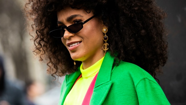 Leila Depina, wearing a neon yellow top, pink suit, green coat, and Chanel earrings 