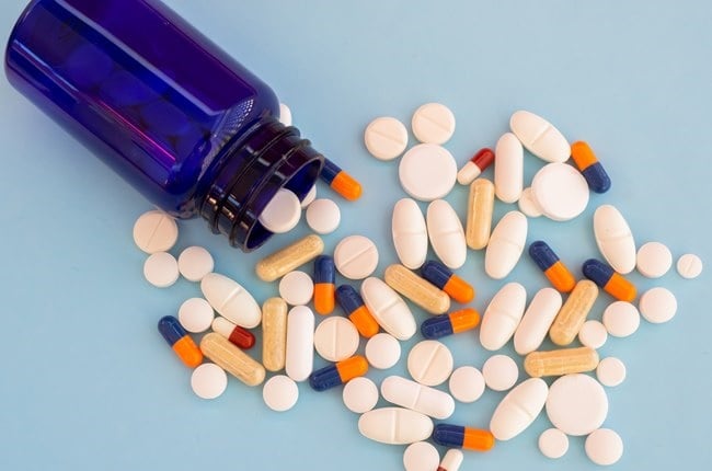 A pile of pills of different sizes, forms and colors on a pastel blue background coming out of a blue jar
