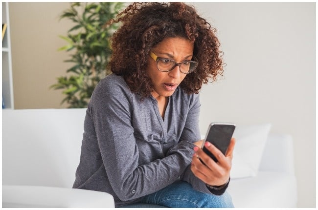 Woman shockingly staring at phone after realising she was scammed online.