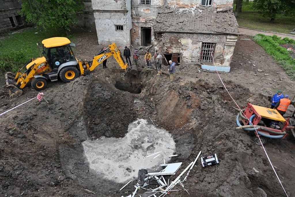 Utility workers next to a crater in the courtyard of a hospital in Kharkiv, on 27 April 2024, after a massive missile strike damaged four power plants. (SERGEY BOBOK / AFP)