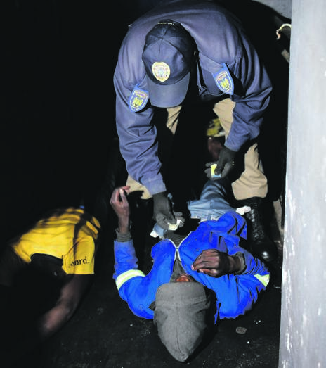 Metro police search suspects during a raid at a derelict building in Braamfontein on Friday night. Picture: Tebogo Letsie
