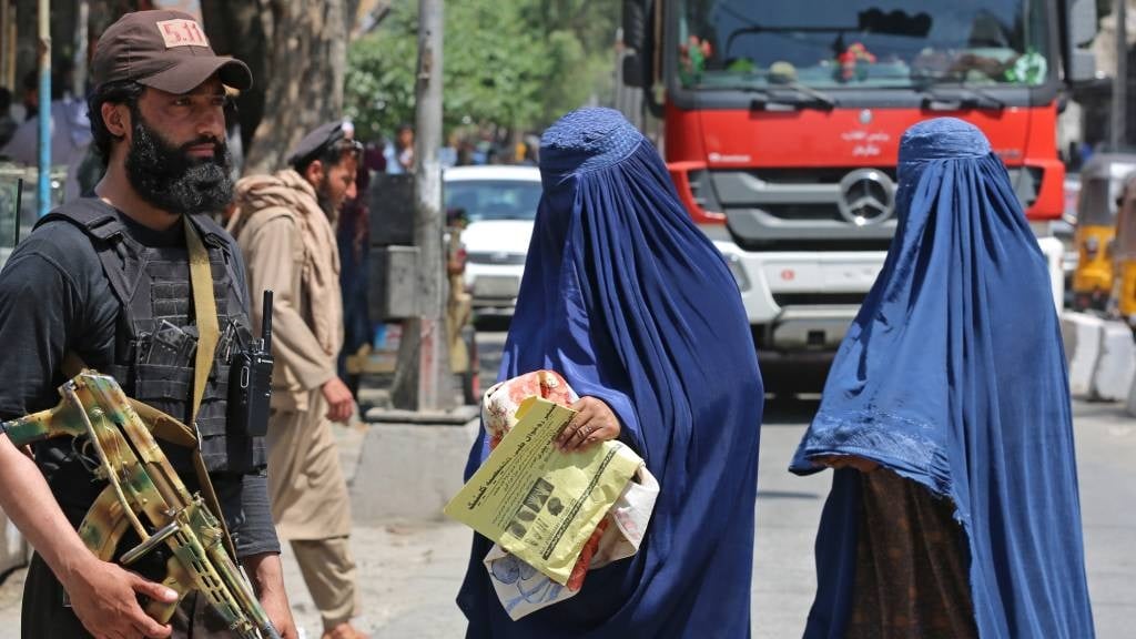 Afghan burqa-clad women walk past a Taliban securi
