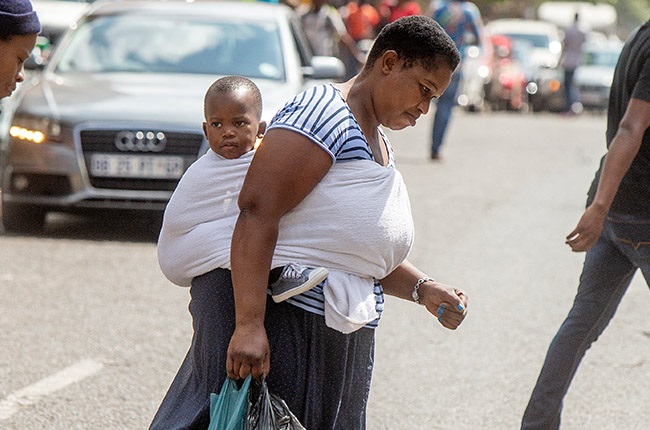 A woman with a baby on her back walking in Hillbrow. 