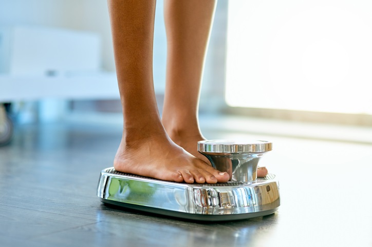 A woman weighing herself with a scale at home. 