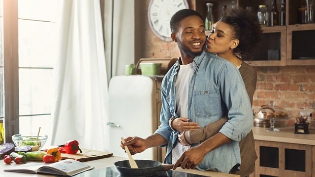 African-american wife kissing husband in kitchen. Family preparing dinner together