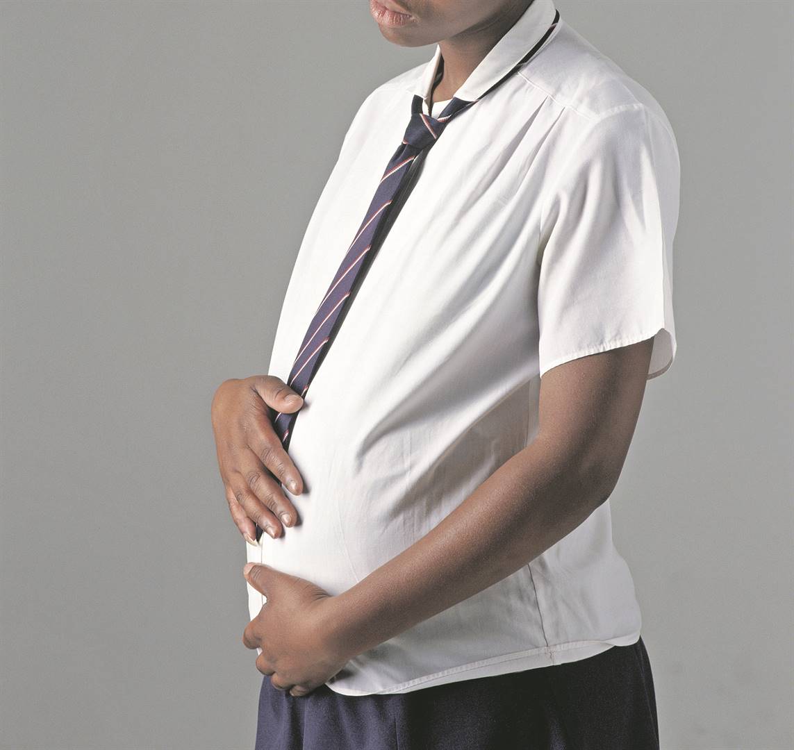 A young pregnant teenager holding her swelling belly and thinking forlornly about her future and imminent motherhood.