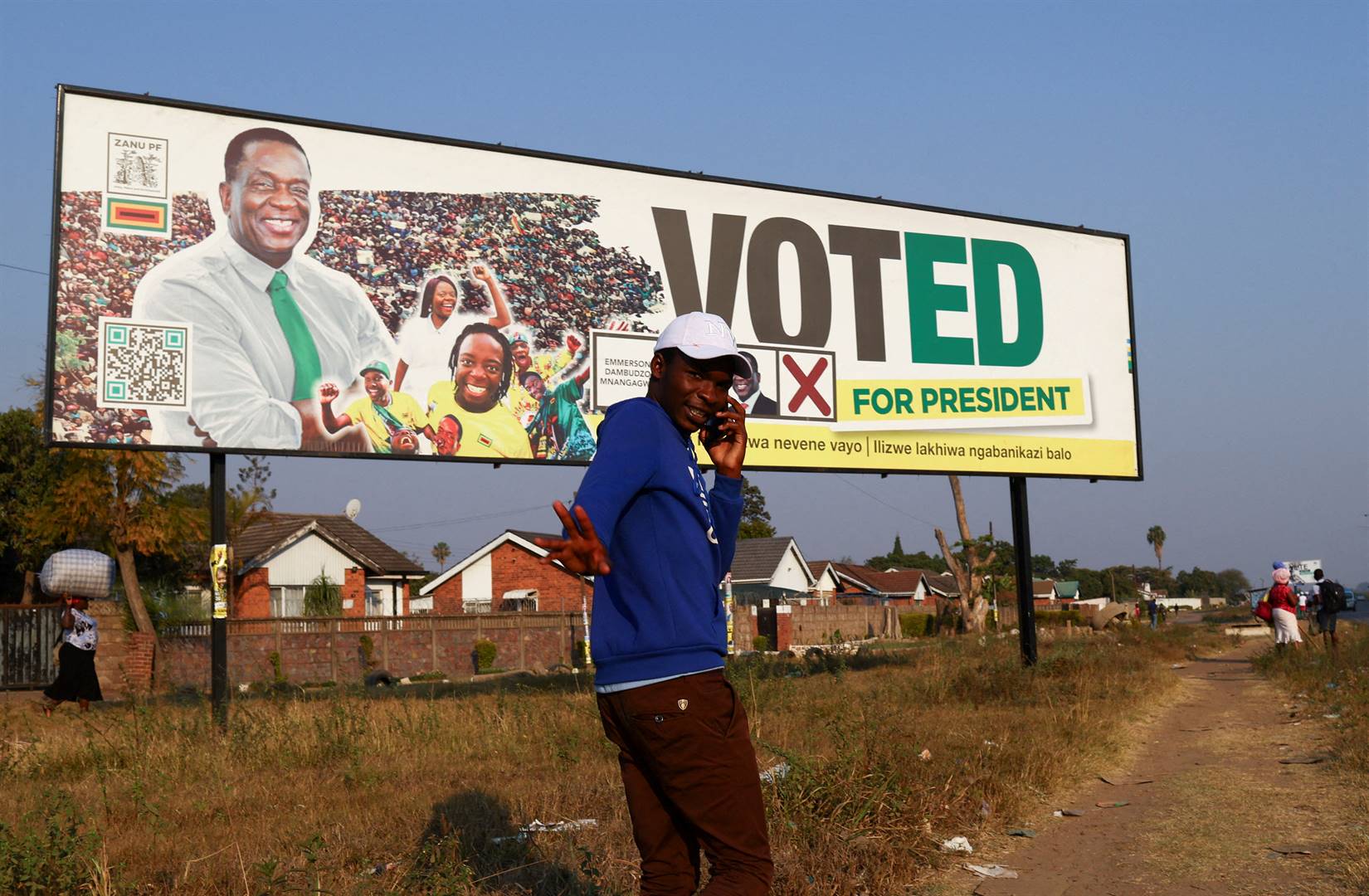 A man gestures while speaking on a cellphone as he walks past a banner of the ruling Zanu-PF party’s President Emmerson Mnangagwa, who was re-elected in the recent presidential elections in Harare, Zimbabwe. 