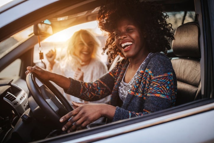 Women having fun on road trip in car at sunset.