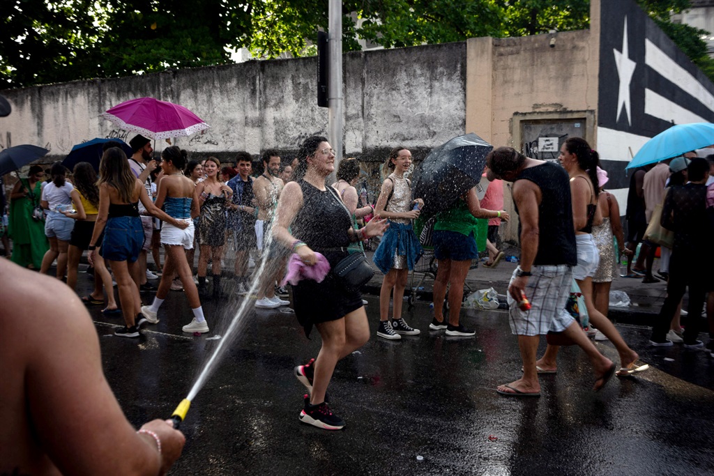 A fan of US singer Taylor Swift cools off with a hose as others queue outside the Nilton Santos Olympic Stadium before Swift's concert, "Taylor Swift: The Eras Tour", amid a heat wave in Rio de Janeiro on 18 November 2023.
