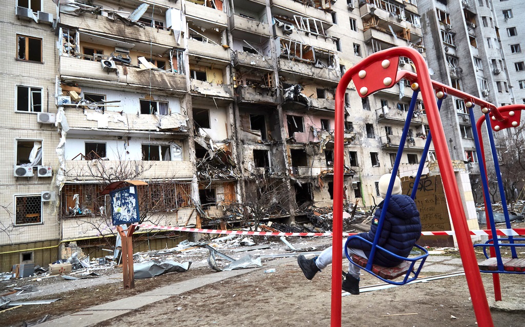 A child on a swing outside a residential building damaged by a missile on 25 February  2022 in Kyiv, Ukraine. 
