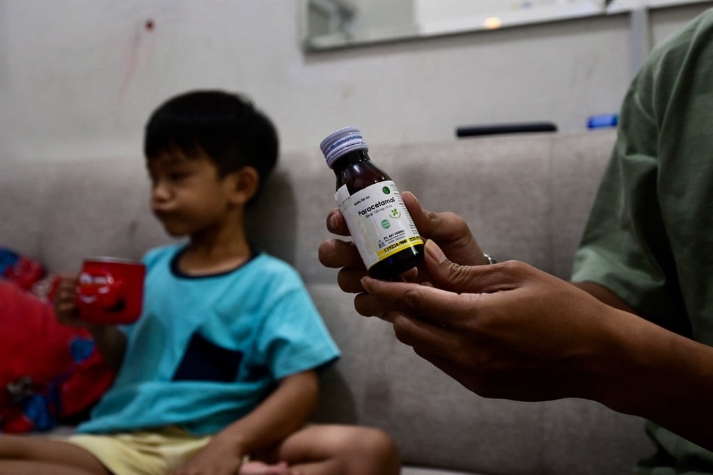 This picture taken on February 11, 2023 shows Riski Agri (R) displaying a bottle of cough syrup that was consumed by his son Farrazka which caused him kidney problems, at their house in Jakarta. 