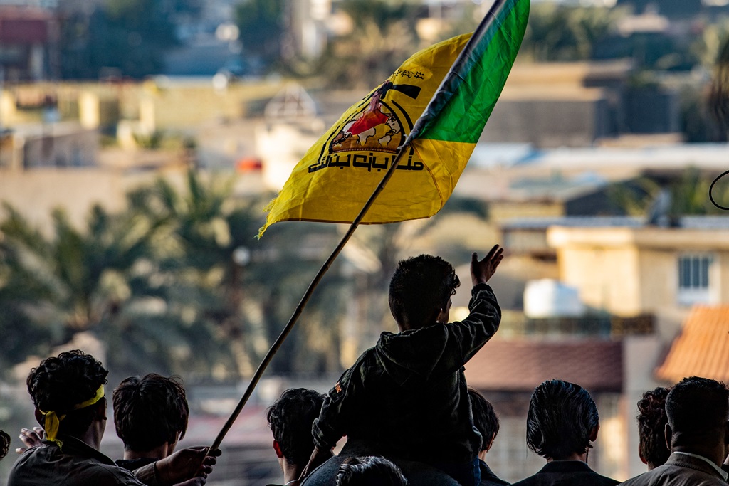 Young men raise the flag of Kataeb Hezbollah (Hezbollah Brigades) group during commemorations marking the second anniversary of the killing of top Iranian commander Qasem Soleimani and Iraqi commander Abu Mahdi al-Muhandis, in the southern Iraqi city of Basra, on 8 January 2022. The 3 January 2020 strike against Soleimani, the architect of Iran's Middle Eastern military strategy, was ordered by then US president Donald Trump, and it also killed his Iraqi lieutenant Abu Mahdi al-Muhandis, the Hashed's deputy chief.