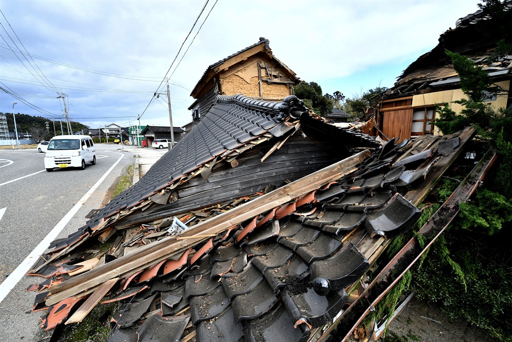 A car passes a collapsed wooden house in Shika Tow