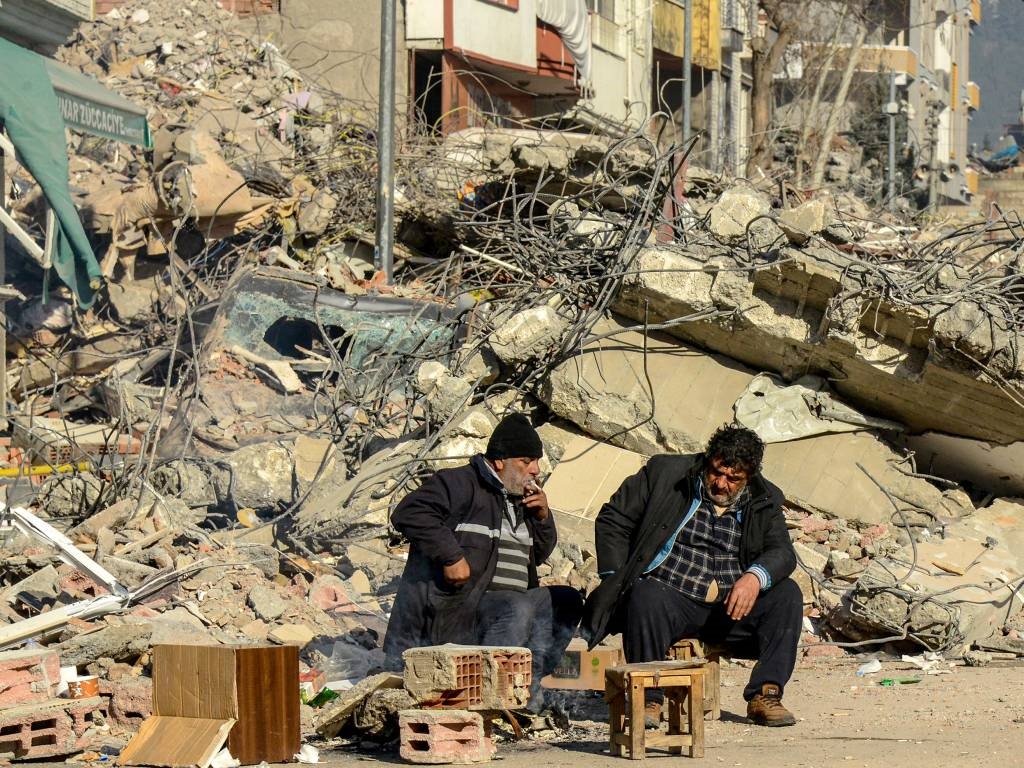 Victims' relatives sit next to the rubble of a col