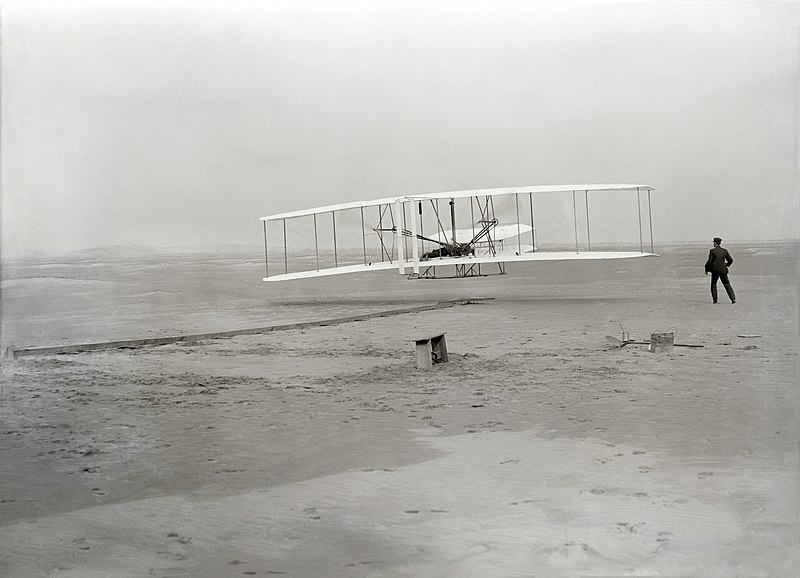 Die eerste vlug van die Wright Flyer op 17 Desember 1903, met Wilbur Wright regs van die vliegtuig. 