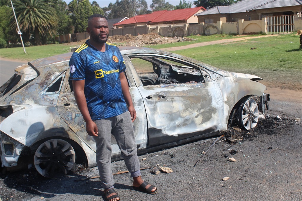 Gold One mine worker Prince Radebe stands next to his burnt car. Photo by Happy Mnguni