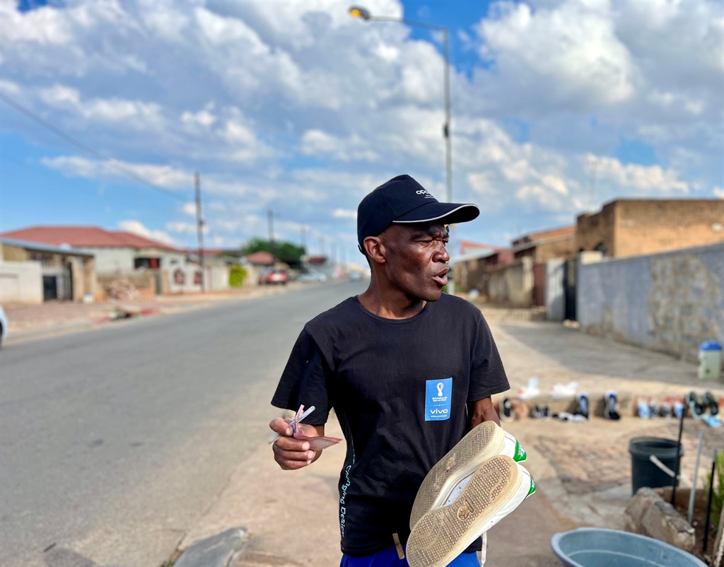 Brian Mokgosi washes sneakers on the street pavement in front of his house