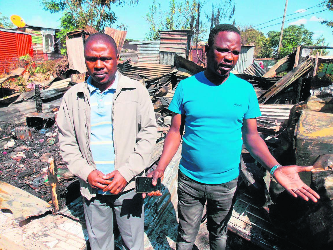 Family members Jackson Zulu (left) and Lazarus Mphela next to the burnt shack, where a fire broke out and killed Joel and Ntombifuthi.  Photo by Raymond Morare